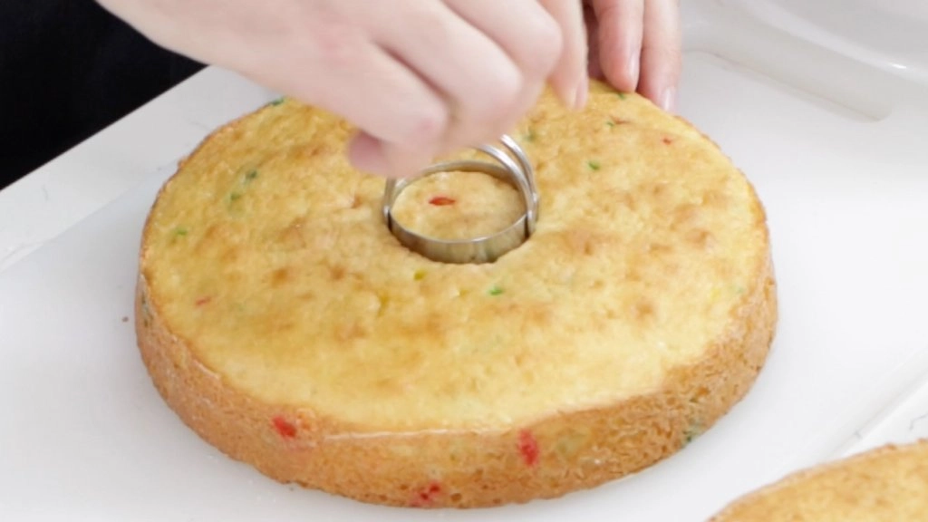 Hand with biscuit cutter taking a hole out of the middle of a cake layer.