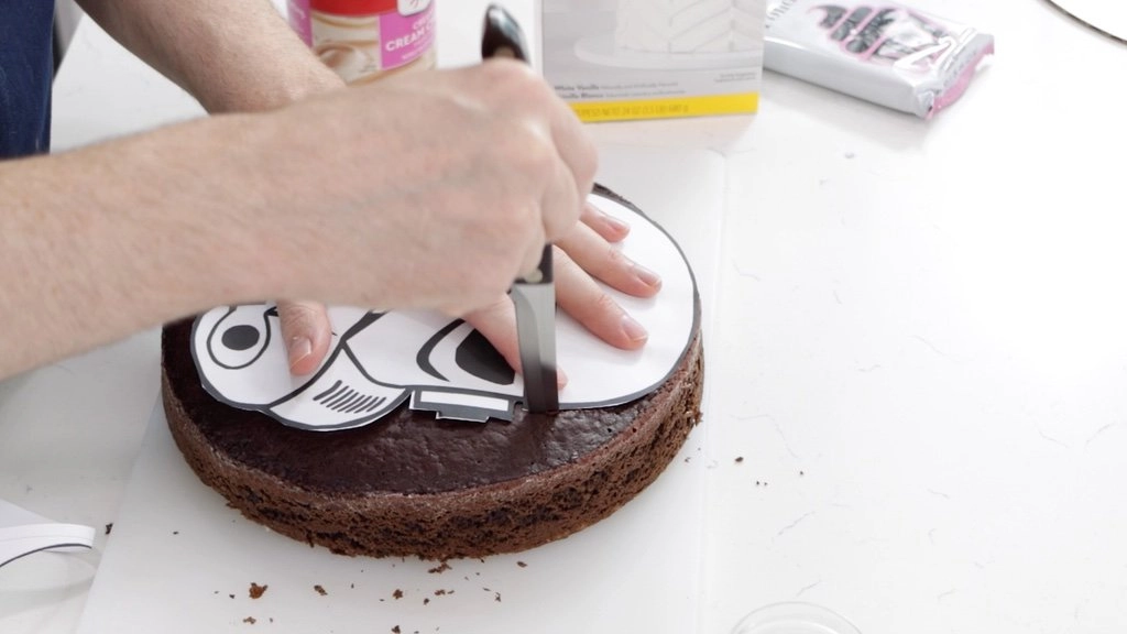 Hand with knife trimming chocolate cake with a stormtrooper stencil