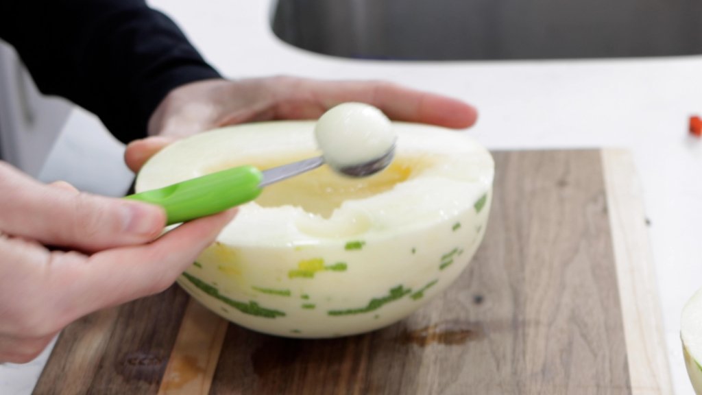 Hand scooping the melon with a melon baller.