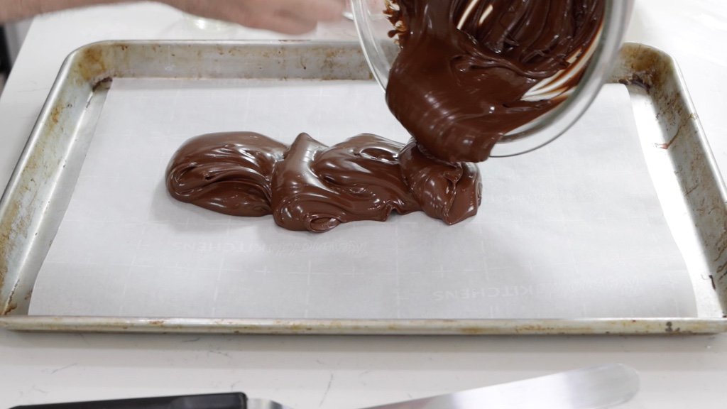 Bowl of melted semi-sweet chocolate being poured on a sheet pan lined with parchment paper.