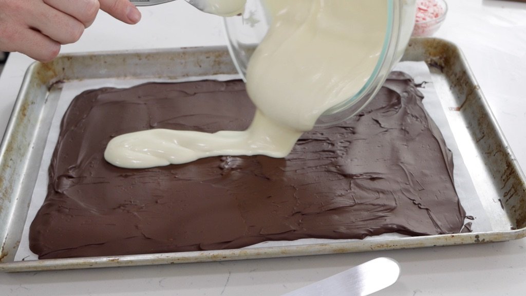 Melted white chocolate being poured on top of a layer of semi-sweet chocolate.