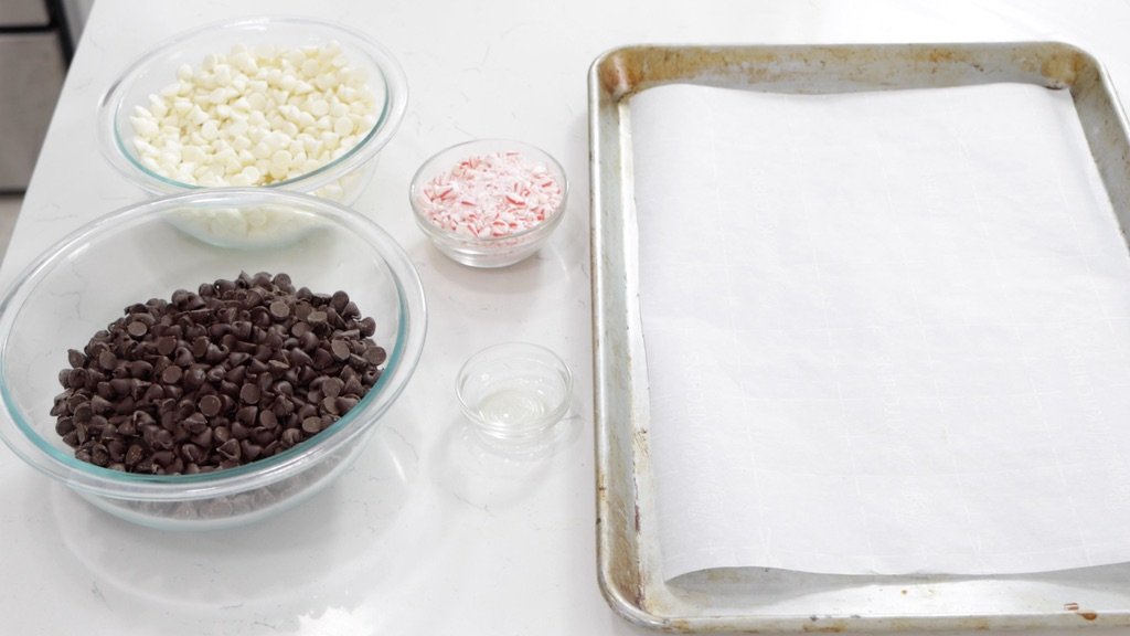 Bowls of chocolate and candy cane next to a sheet pan with parchment paper.