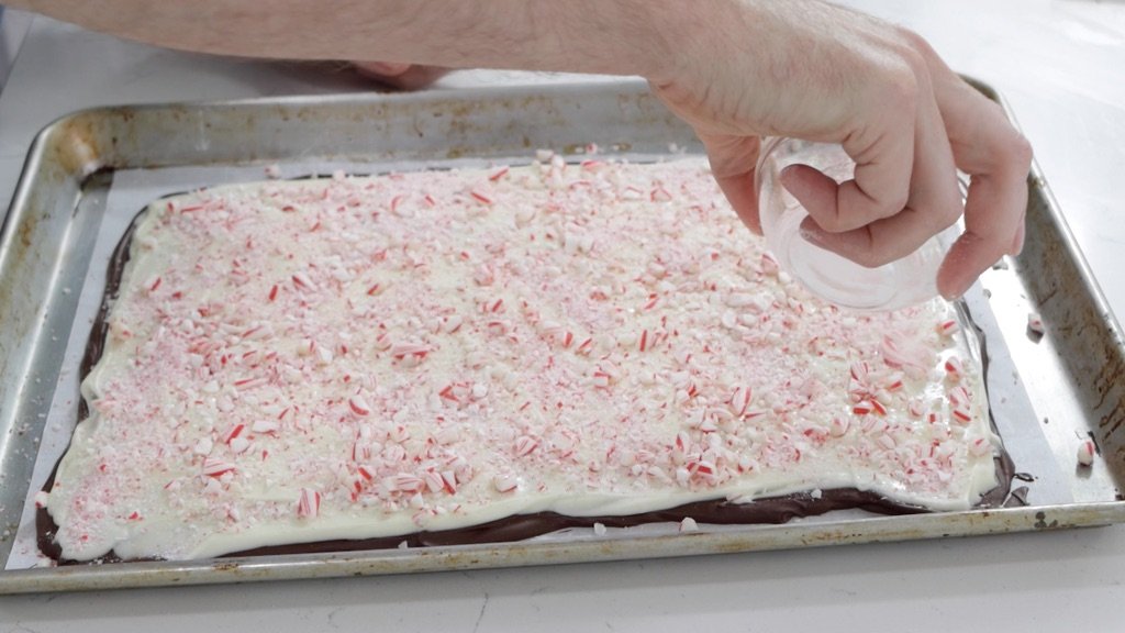 Crushed candy canes being poured on the white chocolate.