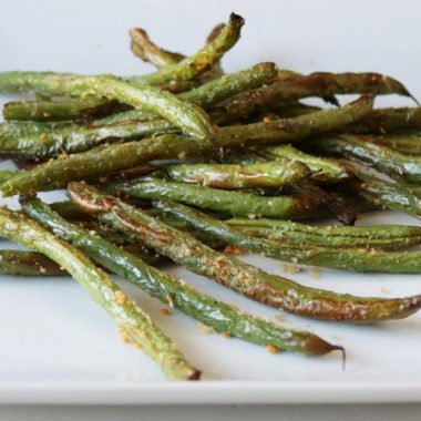 Pile of air fryer green beans on a white plate.