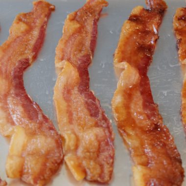 Several strips of bacon on a sheet pan ready for the oven