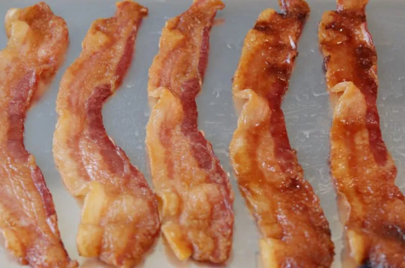 Several strips of bacon on a sheet pan ready for the oven