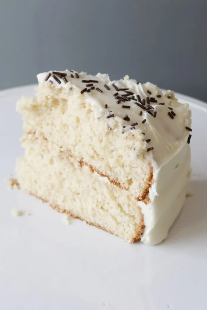 Slice of homemade vanilla cake recipe on a white cake pedestal.