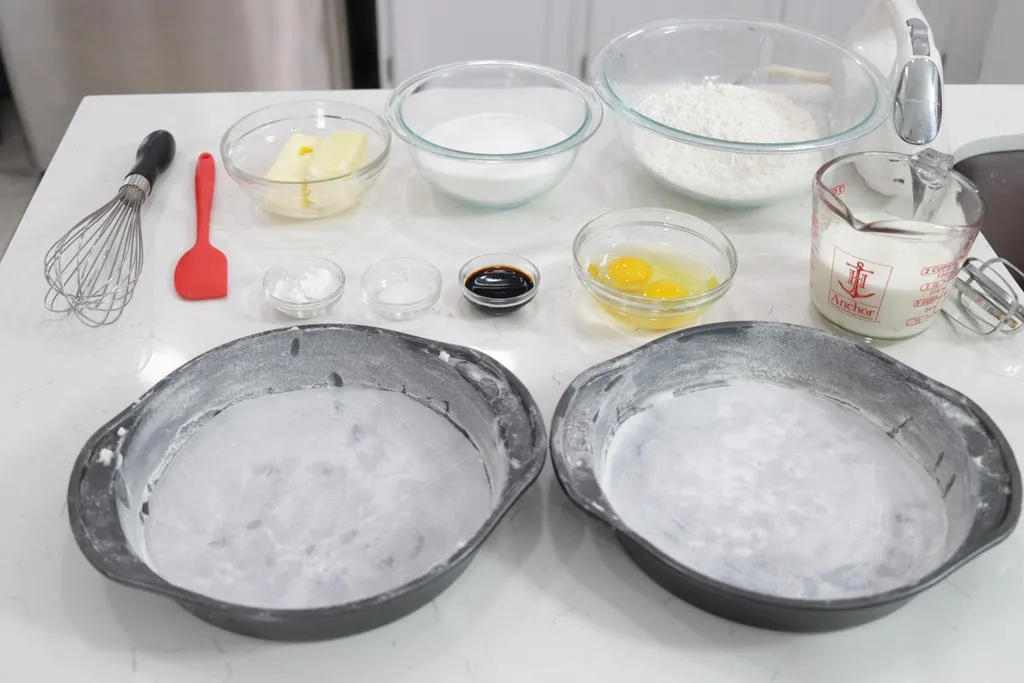 Several ingredients in bowls on top of a white counter next to two 9-inch cake pans.