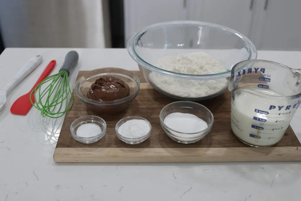 Several ingredients in glass bowls on top of a wooden cutting board.