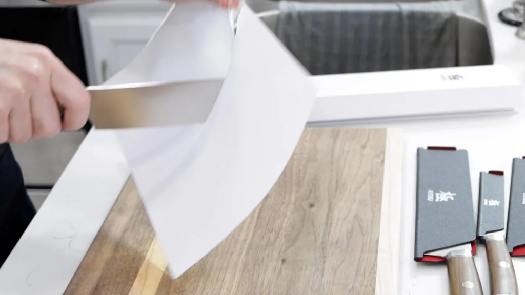 Hand slicing through paper with a Nakiri Kyoku knife.