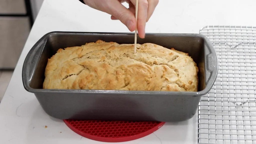 Hand poking freshly baked peanut butter bread with a wooden skewer