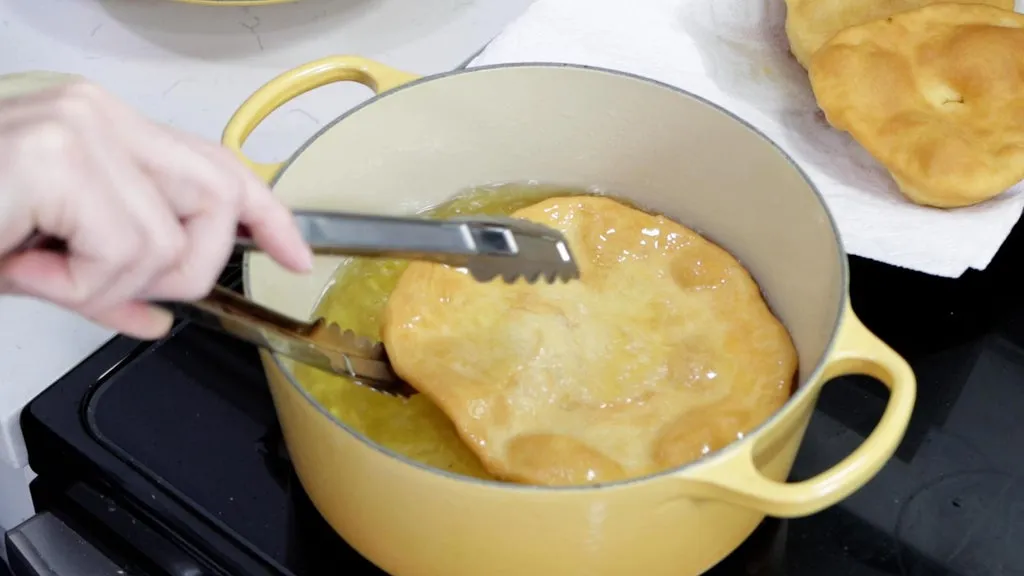 Hand with tongs grabbing finished Indian fry bread out of the oil.