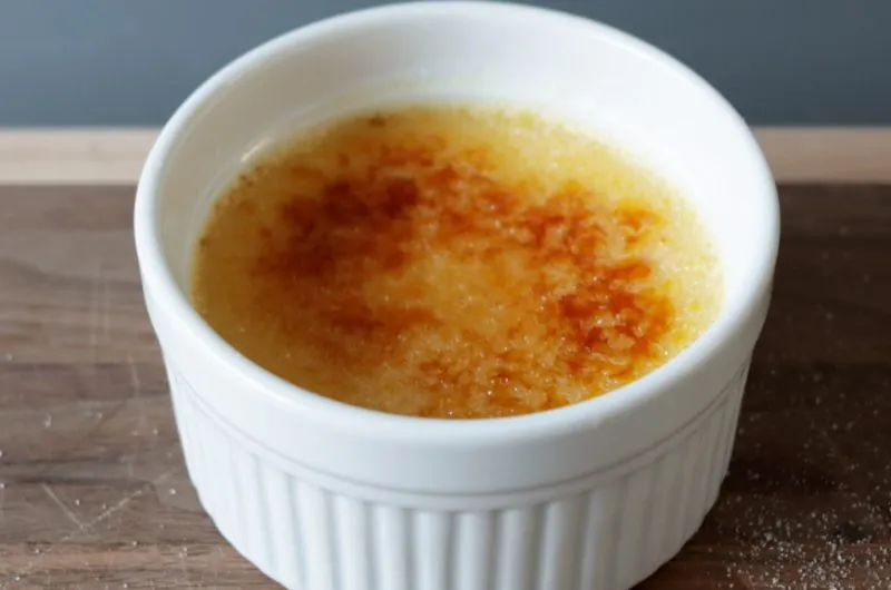 creme brulee in a white ramekin on a wooden cutting board