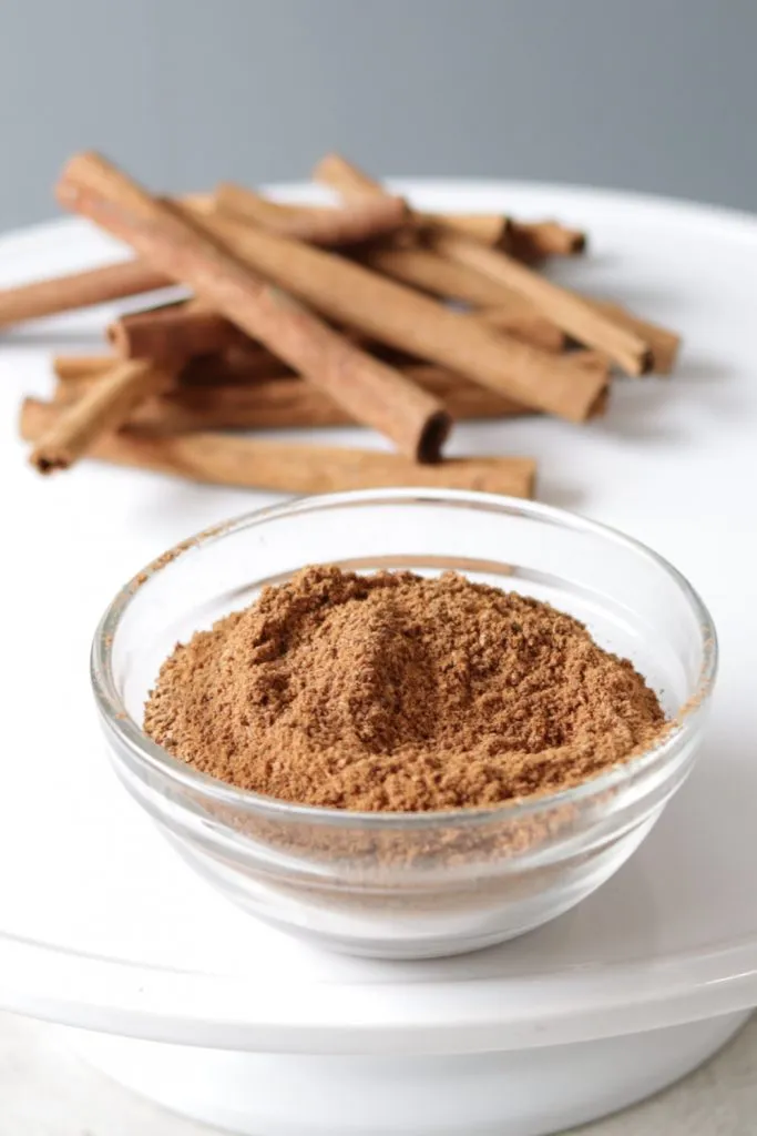 Freshly ground cinnamon next to cinnamon sticks on a white plate.