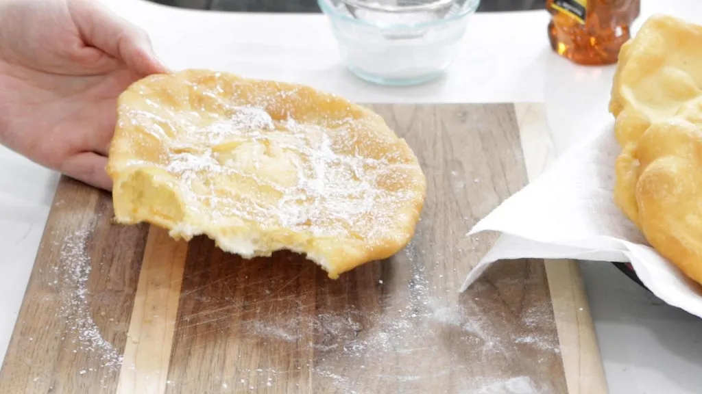 Hand holding a fry bread with honey and powdered sugar on it.