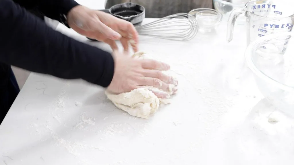 Hand kneading fry bread dough on a counter.