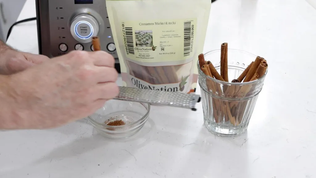 Hand running a cinnamon stick over a Microplane zester into a bowl.