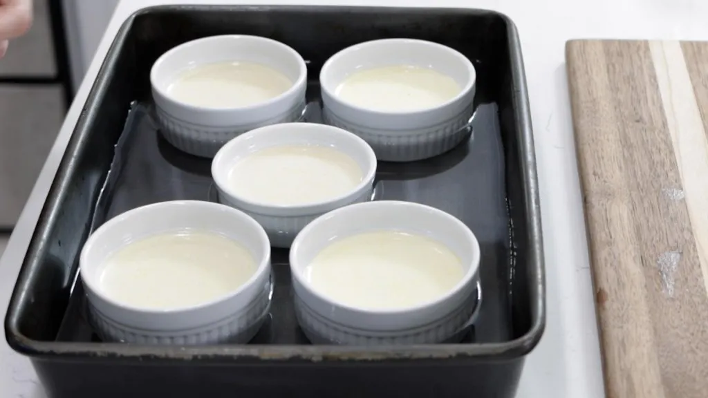 5 ramekins with creme brulee custard in a water bath.