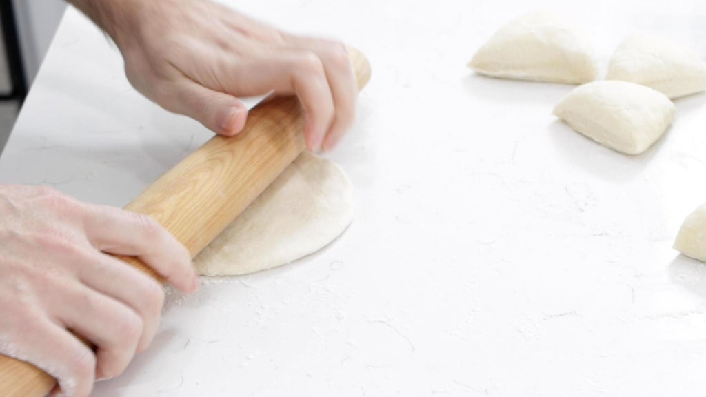 Rolling pin rolling frybread dough on a counter.