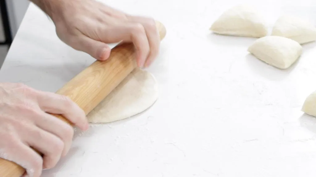 Rolling pin rolling frybread dough on a counter.