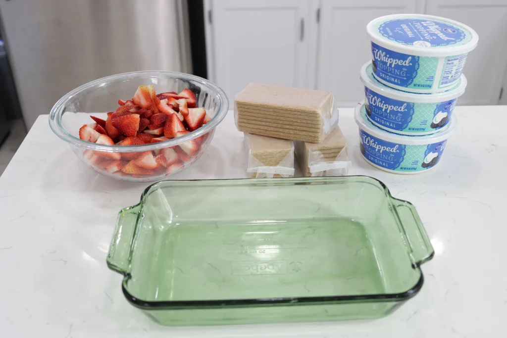Ingredients and tools for strawberry icebox cake on a white counter.