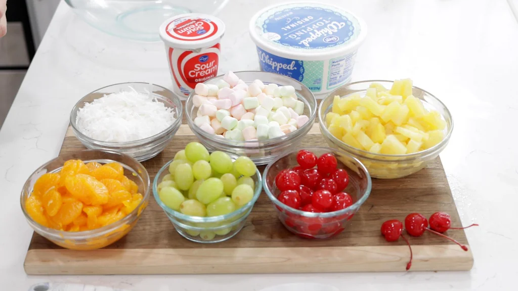 Several bowls of fruit on a wooden cutting board.