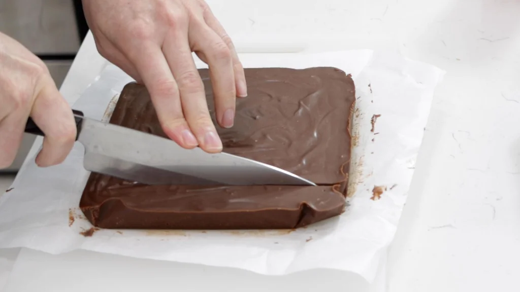 Hand slicing 2 ingredient chocolate peanut butter fudge.