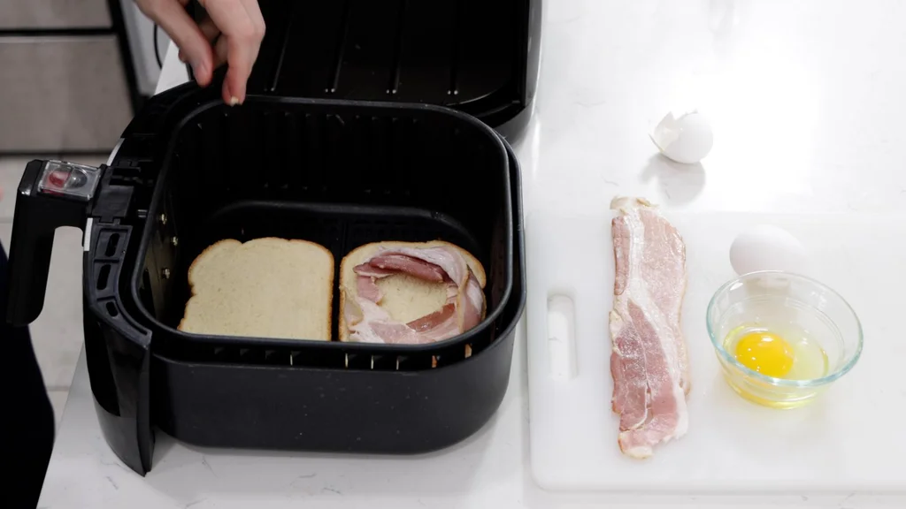 Two slices of bread in an air fryer basket with a curled up piece of bacon.
