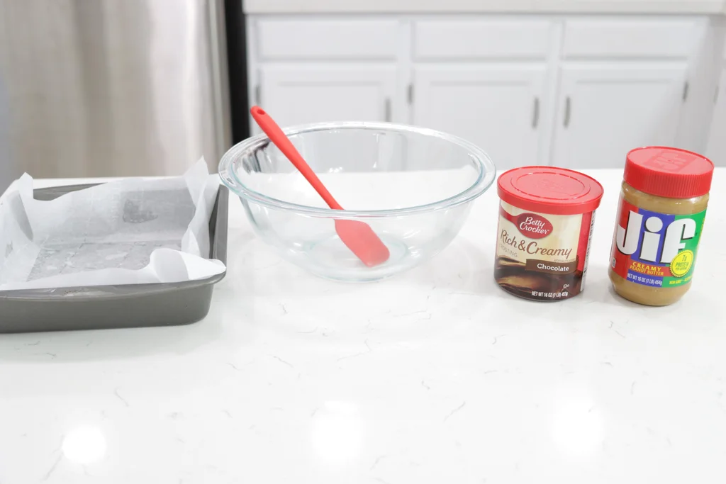 Chocolate frosting and peanut butter on a counter next to a large bowl.