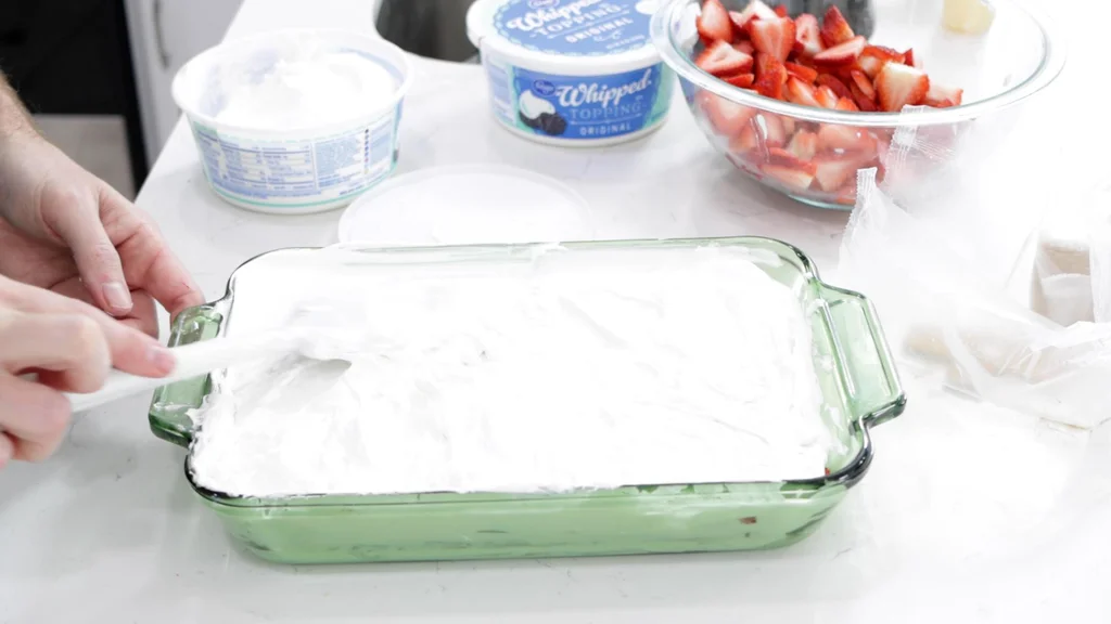 Hand spreading on the last layer of whipped topping for the strawberry icebox cake.