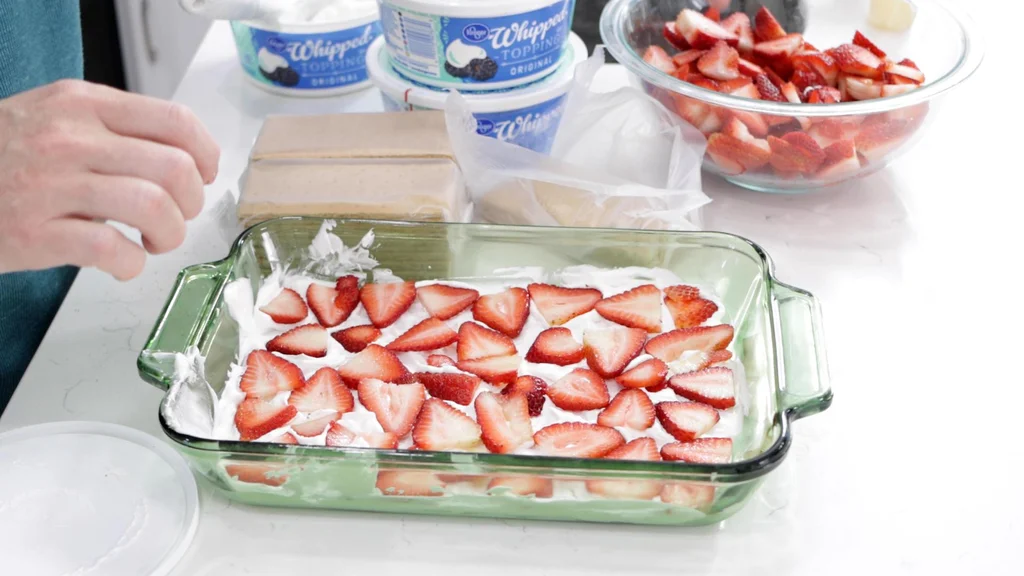 Sliced strawberries on top of whipped cream in strawberry icebox cake.