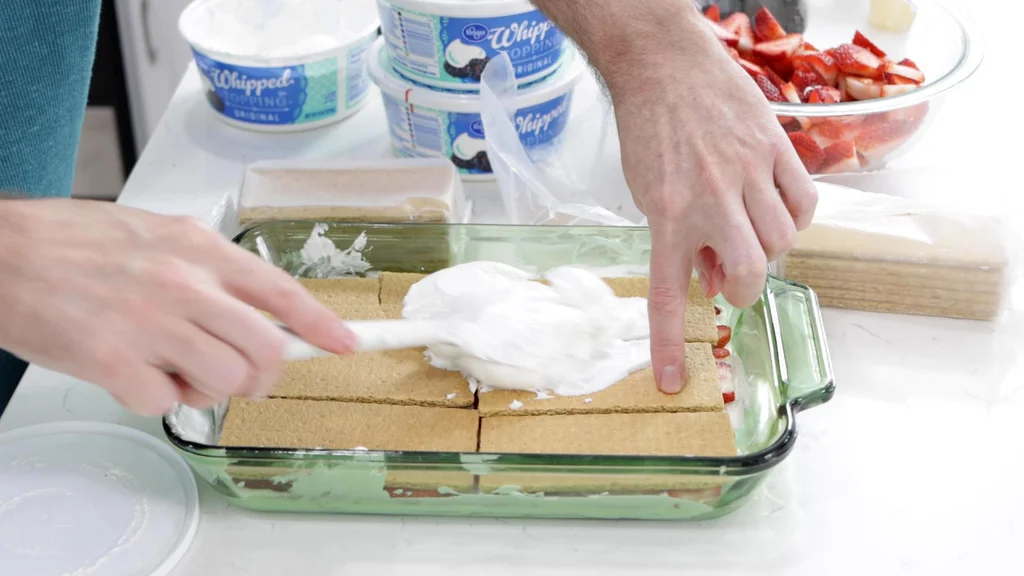Hand holding graham crackers in place while spreading on the whipped cream.