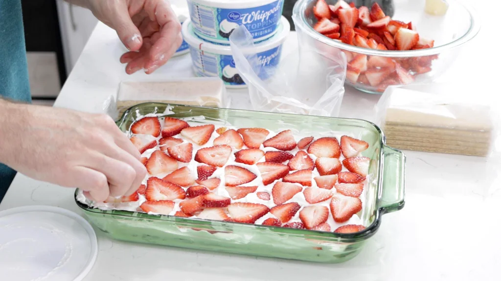 Hand placing sliced strawberries in the middle layer of the icebox cake.