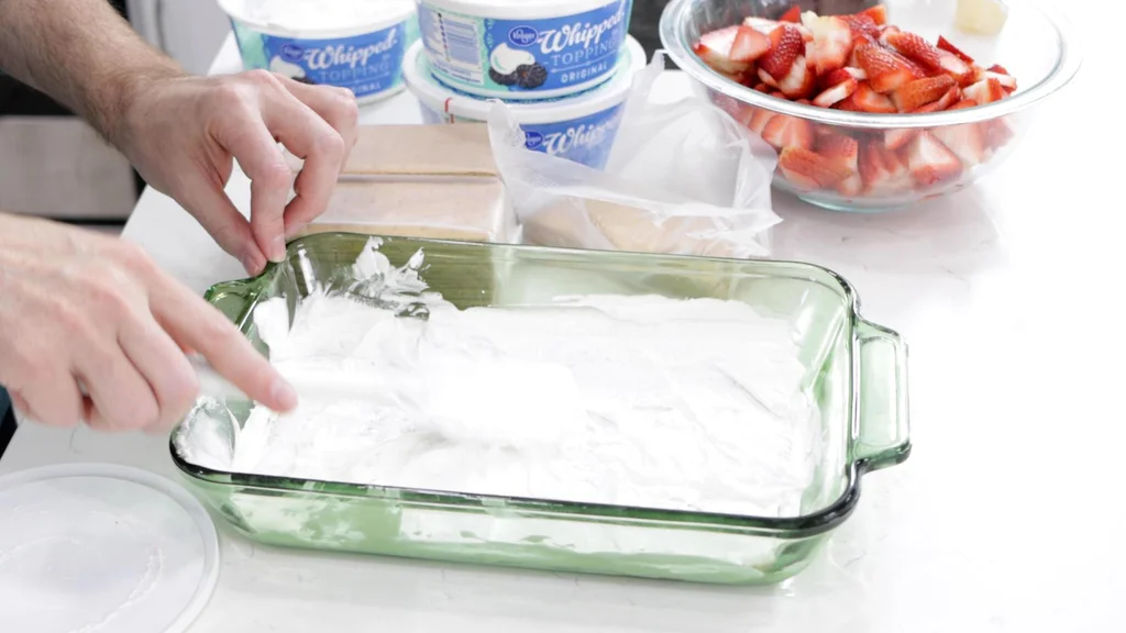 Hand spreading out more cream on the top of the graham crackers.