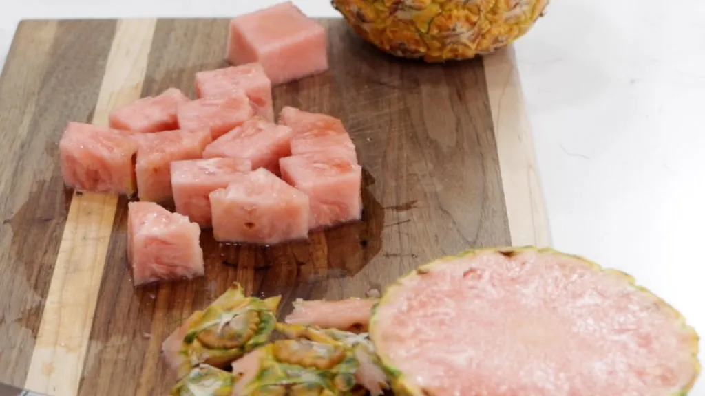 Pink pineapple chunks on a wooden cutting board.