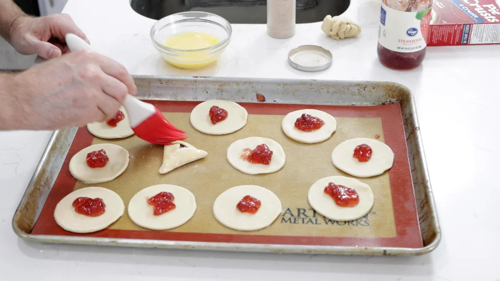 Hand with basting brush, brushing the tops of the unbaked hamantaschen