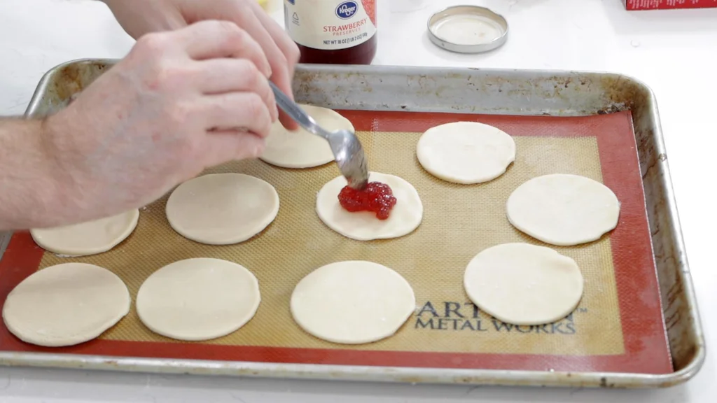 Spoon placing jelly in the middle of round pieces of pie crust dough.