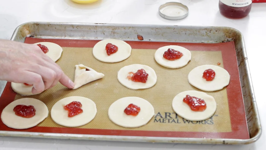 Folded unbaked hamantaschen on a sheet pan.