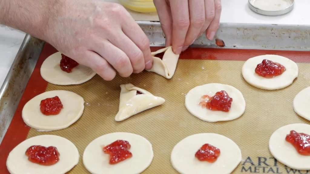 Hands pinching shut some hamantaschen.