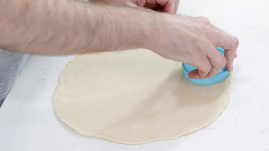 Hand with a circle cookie cutter, cutting out circles of pie crust dough.