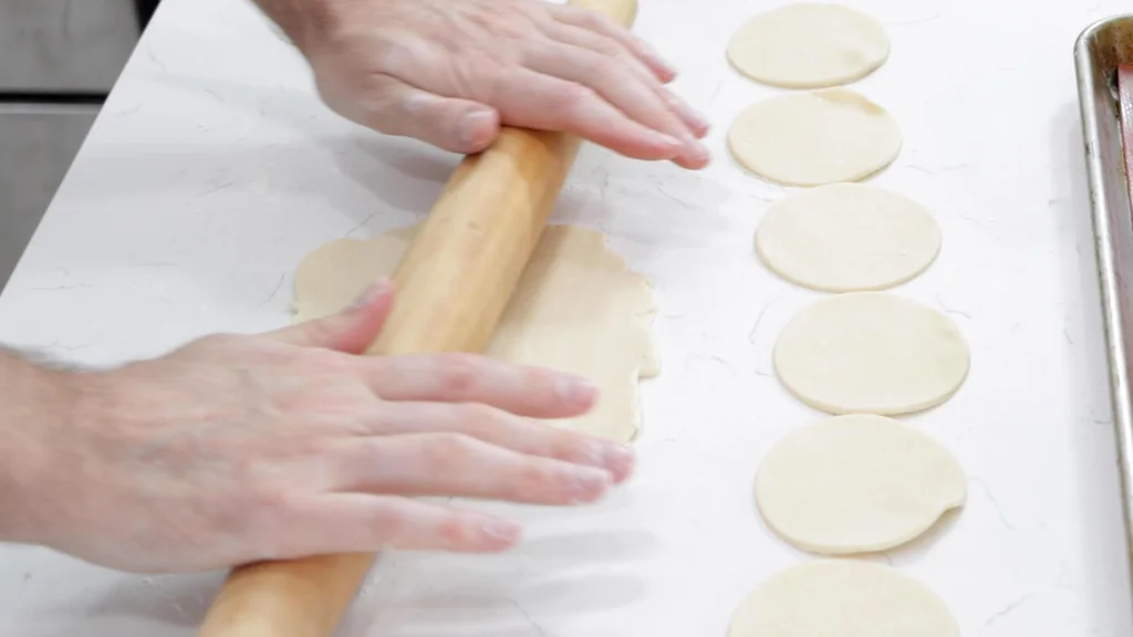 Hands rolling pie crust dough flat.