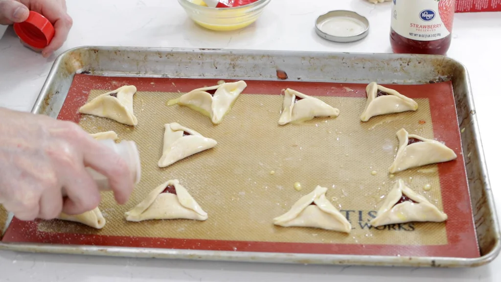 Hand sprinkling cinnamon and sugar on the hamantaschen pie crust cookies