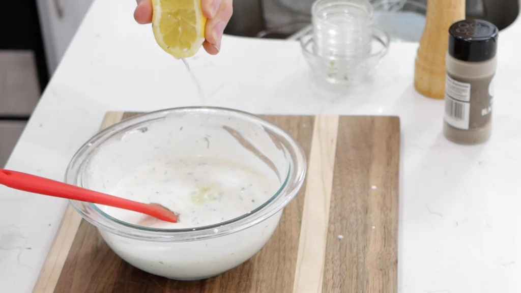 Hand squeezing some lemon juice into a bowl of ranch dressing.