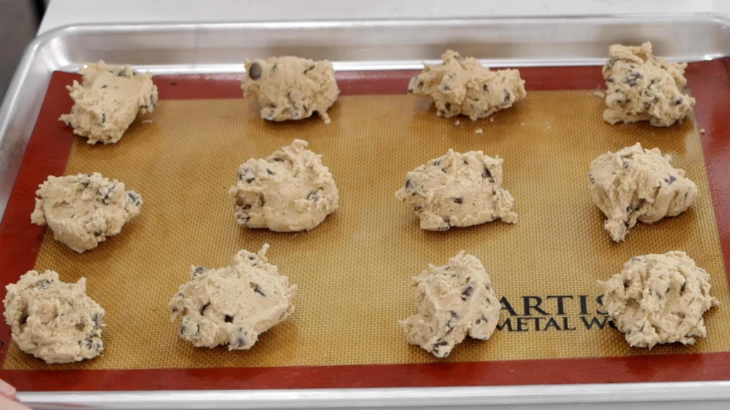 Balls of chocolate chip cookie dough on a cookie sheet ready to be baked.