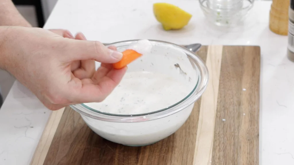 Hand dipping a carrot in fresh homemade ranch dressing.