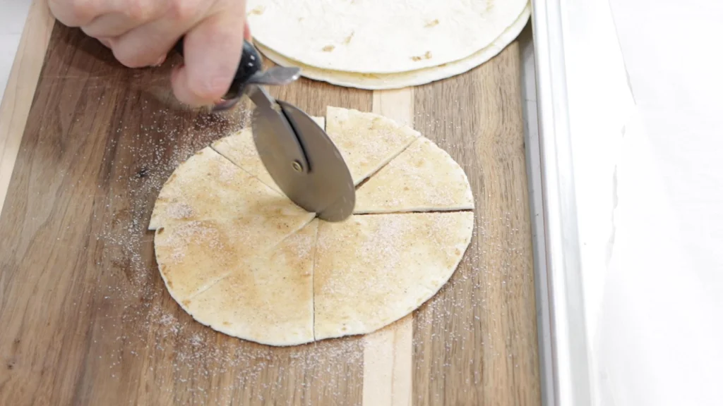 Hand with pizza roller cutting tortillas into wedges.
