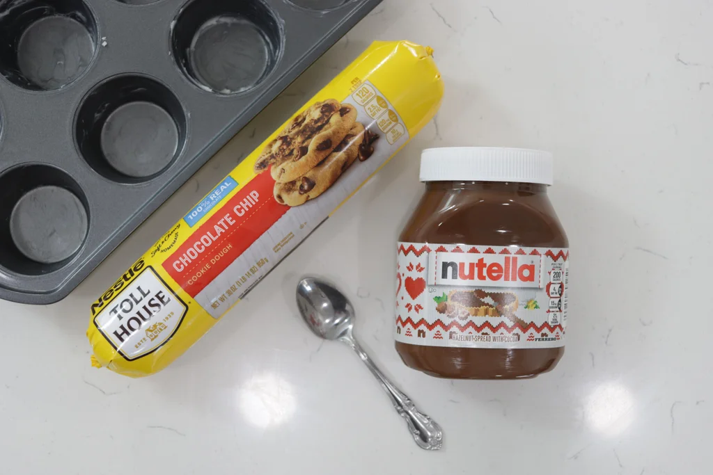 Package of chocolate chip cookie dough and container of Nutella on a counter.