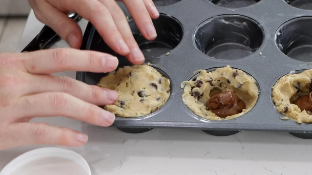 Placing cookie dough on top of the unbaked cookie cups