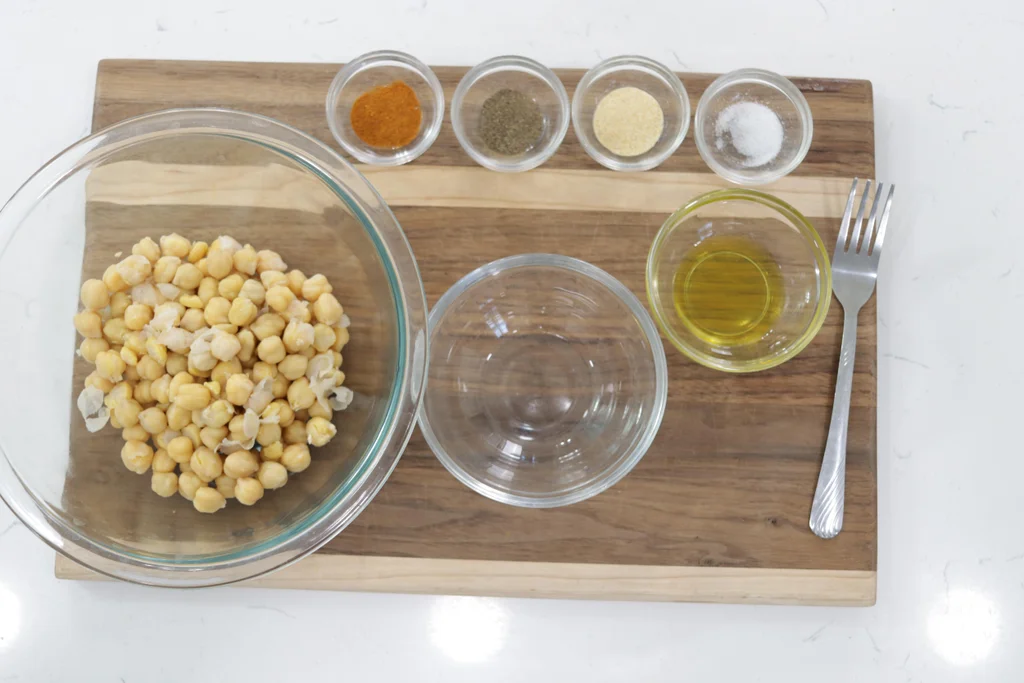 Bowl of canned garbanzo beans next to small bowls filled with spices.
