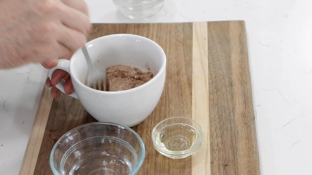 Hand mixing mug cake dry ingredients in a white mug.